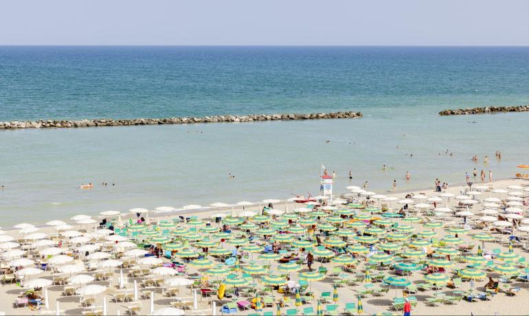 Plage bondée avec des parasols colorés et une mer calme.