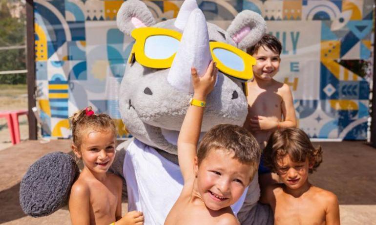 Bambini sorridenti con una mascotte in costume da rinoceronte.