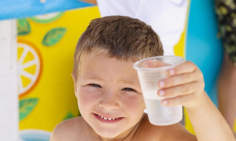 Bambino sorridente con bicchiere d'acqua al chiosco colorato.